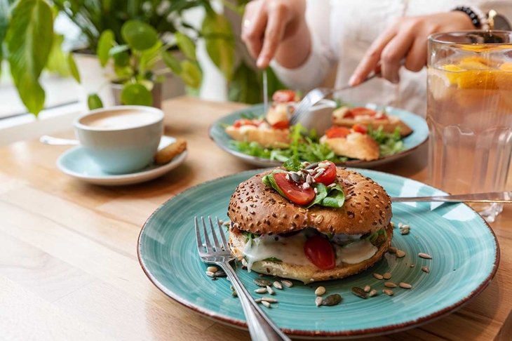 Vegetarian food on plate and cutlery on a table in restaurant with hands of woman. Vegan lunch with roll and vegetables with coffee. Helathy fresh breakfast. Close up.