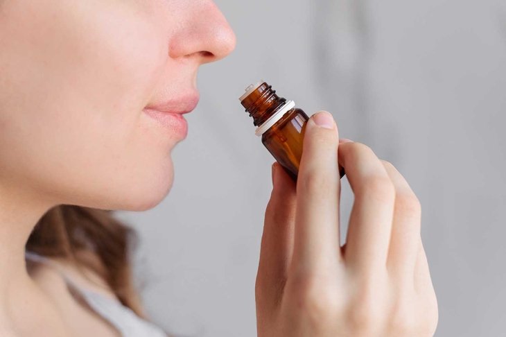 Aromatherapy: a girl with beautiful skin holds a bottle of essential oil near her nose and inhales. Close up, bright marble background.