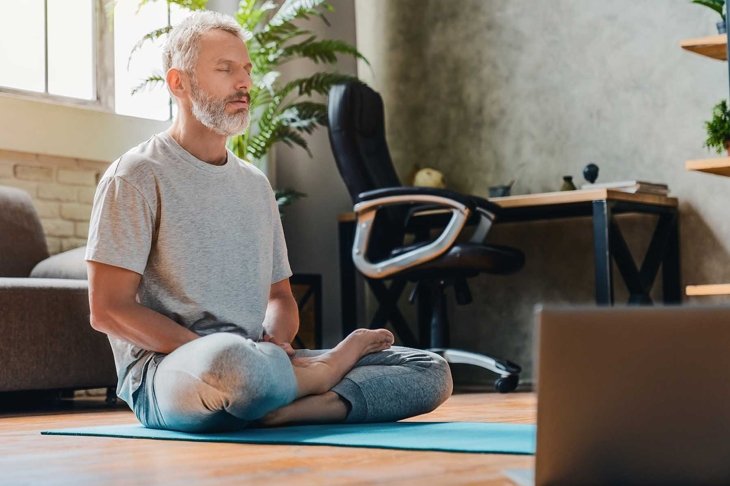 Middle aged sport man doing yoga and fitness at home using laptop