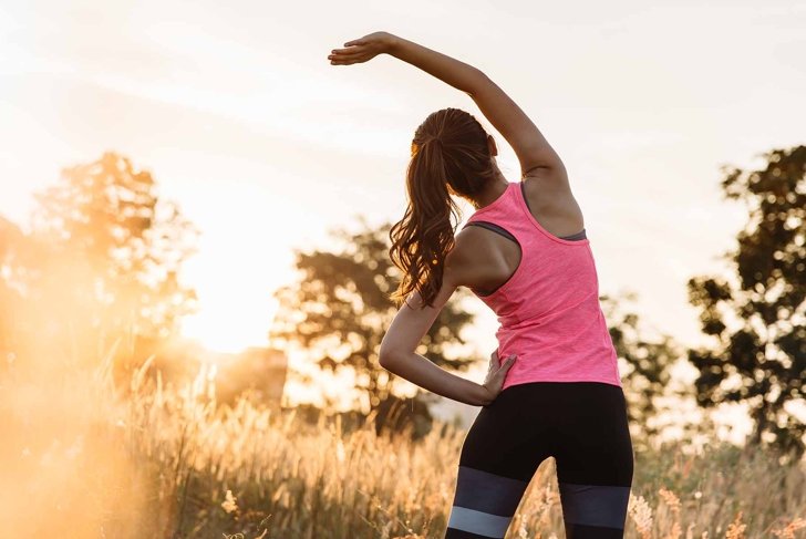 Young female workout before fitness training session at the park. Healthy young woman warming up outdoors. She is stretching her arms and looking away,hi key.