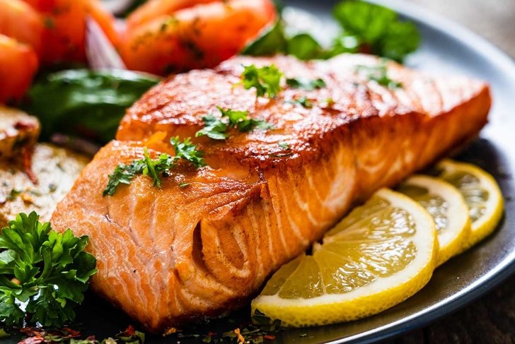 Fried salmon steak with potatoes and vegetables on wooden table