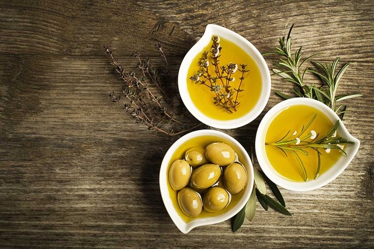 Olive oil with fresh herbs on wooden background.