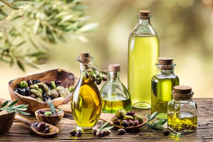 Olive oil and olive berries are on the wooden table under the olive tree.