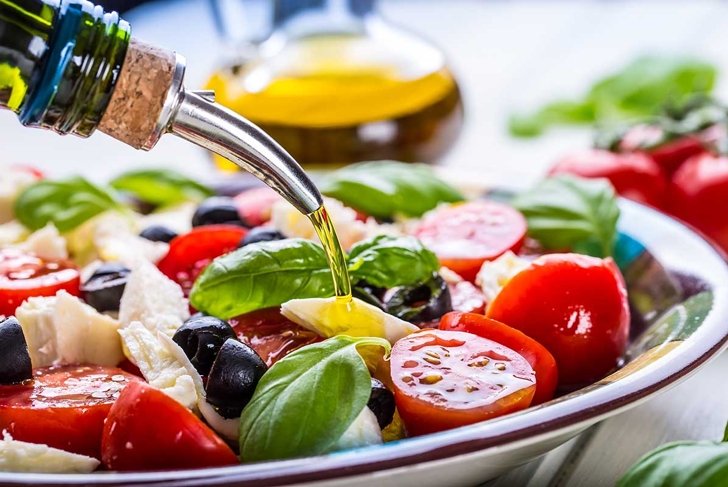 Caprese Italian or Mediterranean salad. Tomato mozzarella basil leaves black olives and olive oil on wooden table.