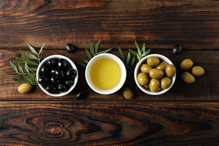 Bowls with olives and oil on wooden background, space for text