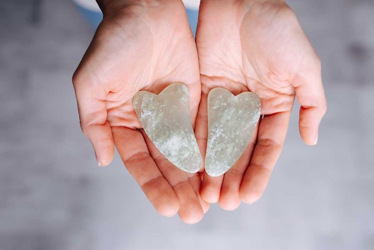 Hands presenting gua sha stones over grey floor. Top view. River jade shaped in a special way for a traditional chinese face massage.