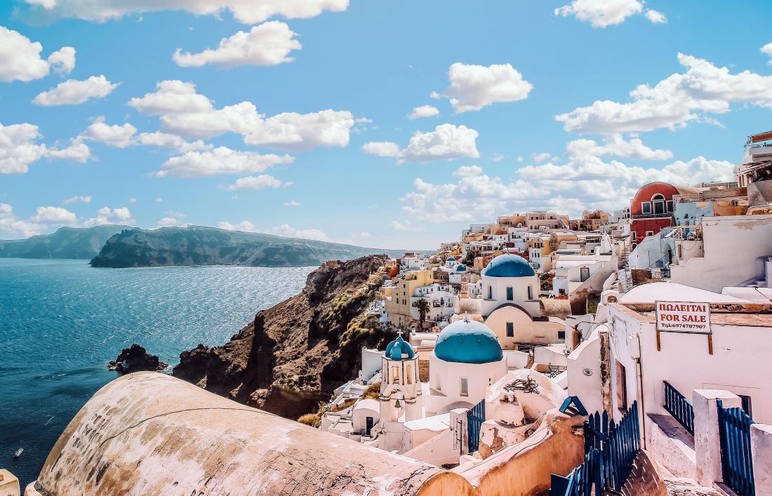 Whitewashed buildings with blue roofs along a hilly coastline leading down to the water