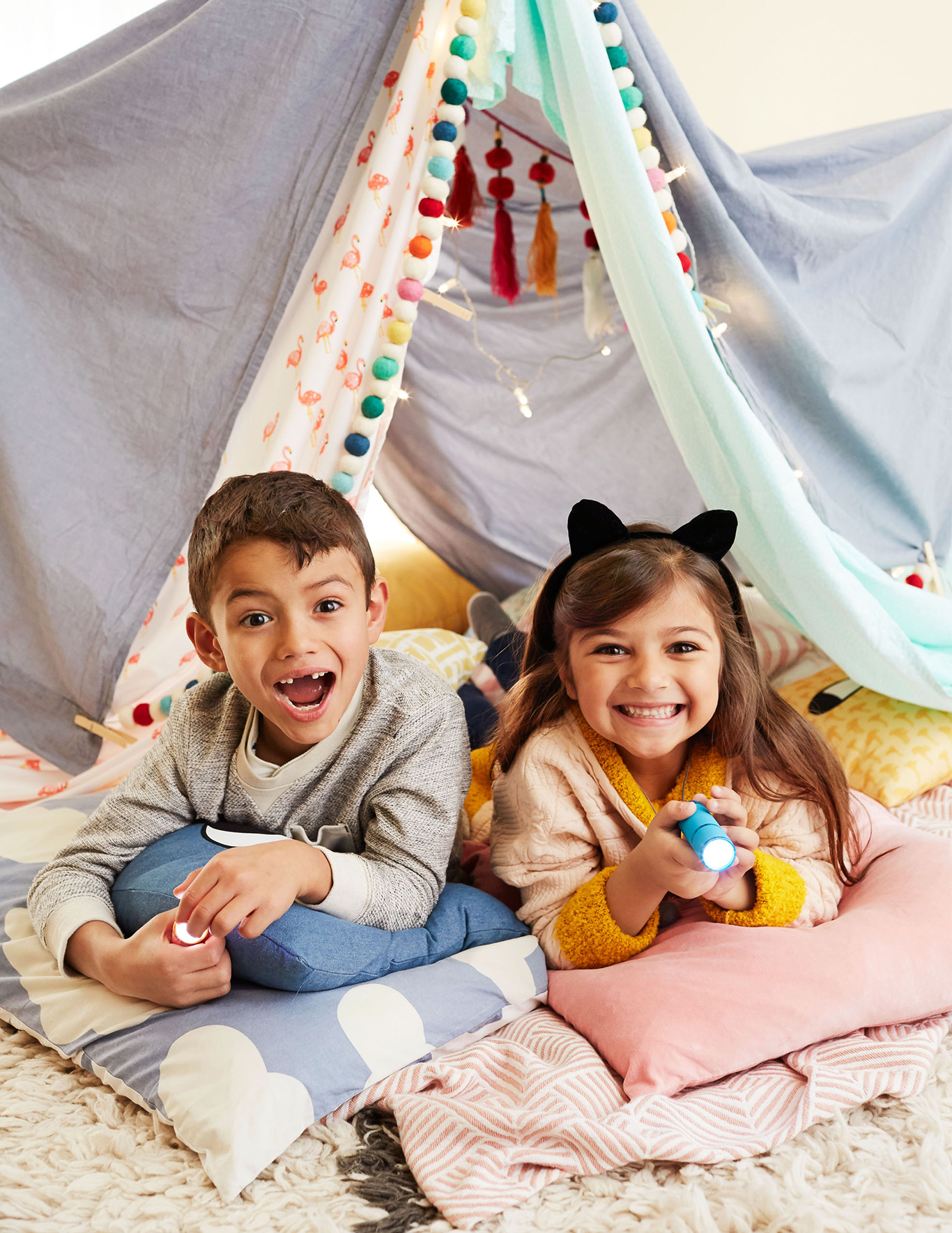 boy and girl on pillows with flashlights under a blanket fort